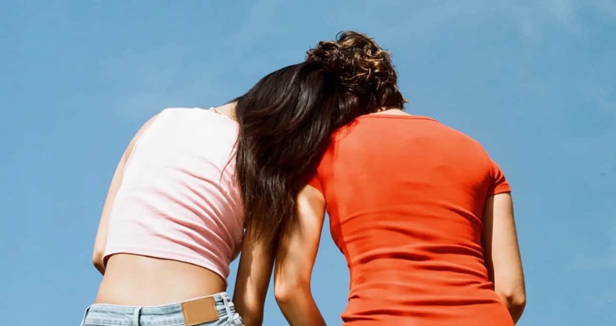 Photo from behind of two young women leaning on each other