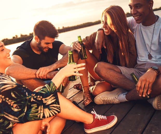 Stock photo of two men and two women laughing and smiling together while drinking on a pier