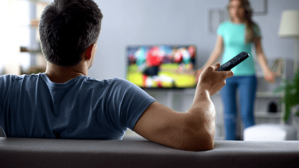 Stock photo of a man watching TV while woman is upset