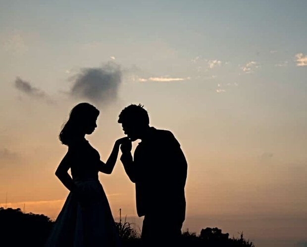 Photo of the silhouettes of a man kissing a woman's hand