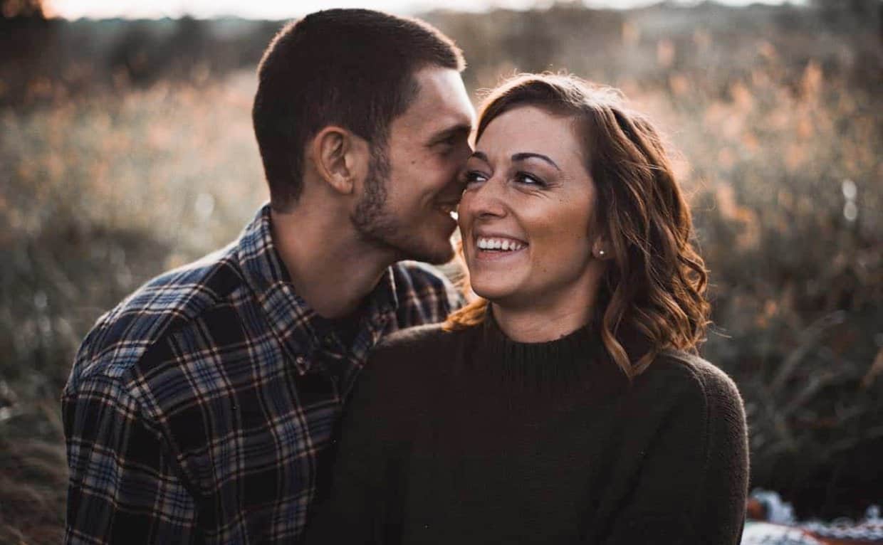Photo of a man and woman laughing and cuddling in a field