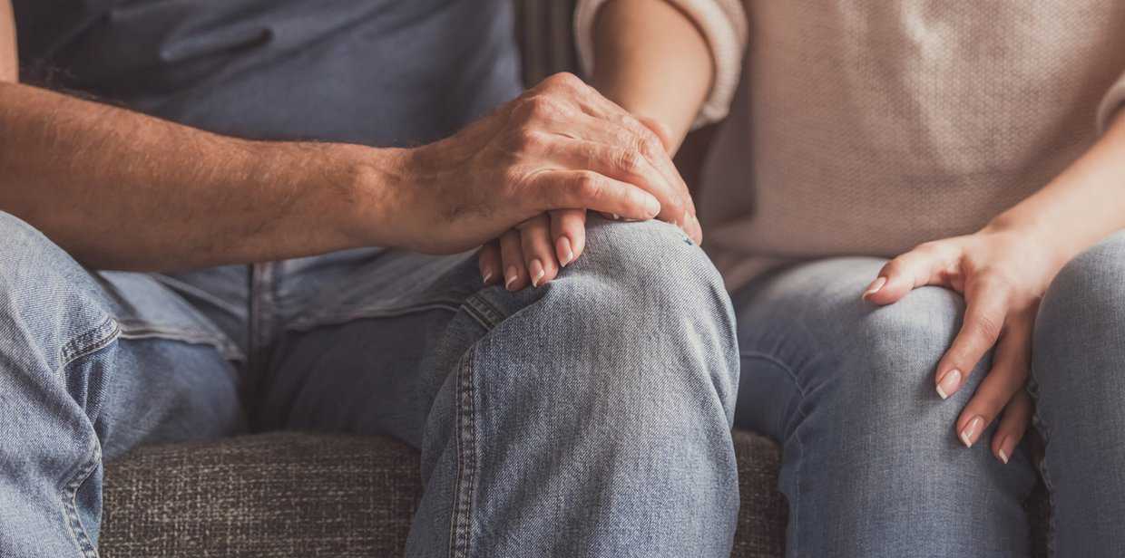 Close-up photo of a couple holding hands while sitting on a sofa.