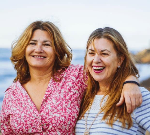 Photo of two women friends standing and smiling with their arms around each other