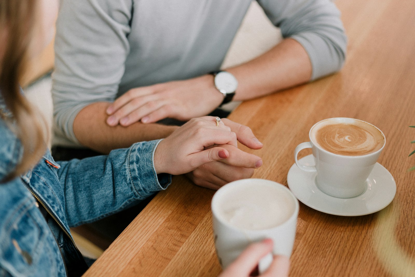 Two people holding hands across a cafe table next to coffee cups