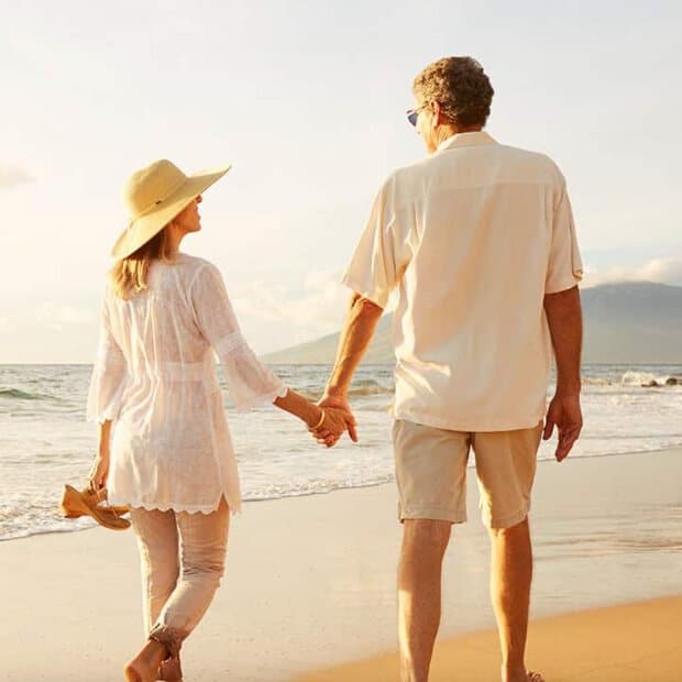 Photo of older couple holding hands and walking on beach