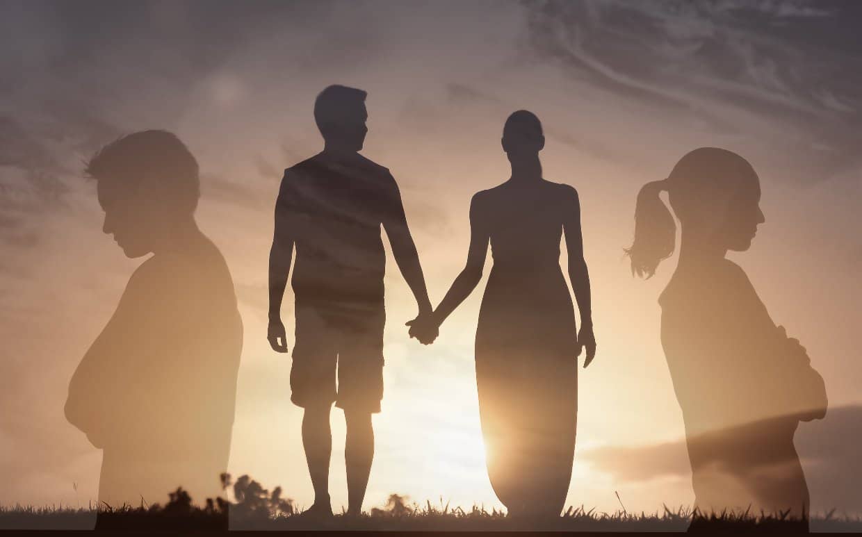 Photo of Couple Silhouettes Walking And Holding Hands. The couple stands back to back with their arms crossed on either side of the walking couple.