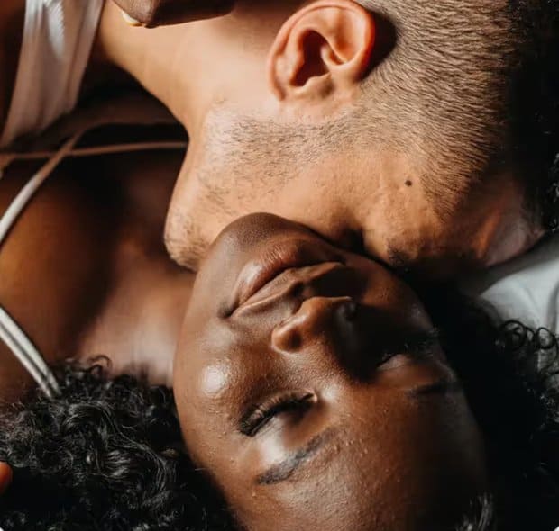 Photo of a young man kissing a young woman's neck while the woman closes her eyes and smiles